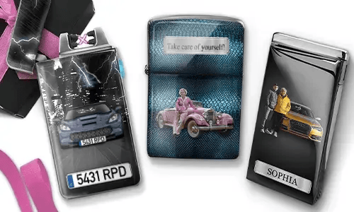 Three metal lighters featuring personalized designs. The left lighter shows a city skyline and a couple beside a car with 'BESTE OMA DER WELT'. The middle lighter depicts a pink vintage car with 'HAB DICH LIEB OMA' above. The right lighter displays a blue car and a license plate. Pink ribbons add a gift-like context.