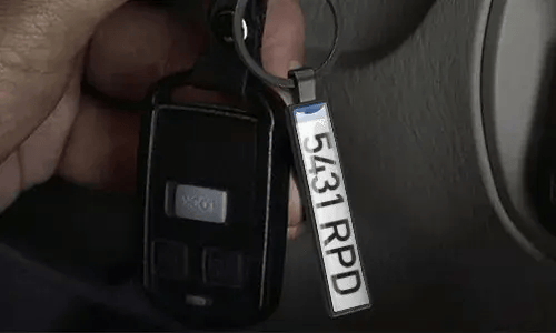Silver license plate keychain hangs from car keys inside a vehicle