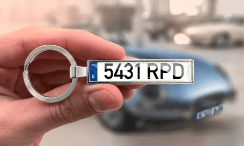 Schlüsselanhänger mit individuellem Nummernschild, in der Hand gehalten, mit Auto im Hintergrund