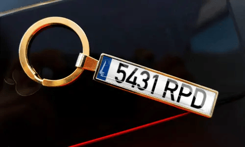 Nummernschild-Schlüsselanhänger an Schlüsseln in der Tasche, mit Auto im Hintergrund