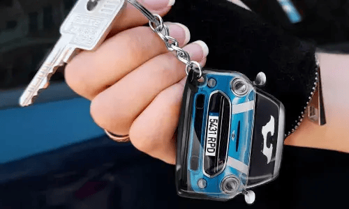 Hand som håller en nyckelring i form av en blå bil med detaljerad frontdesign