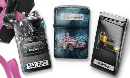 Three metal lighters featuring personalized designs. The left lighter shows a city skyline and a couple beside a car with 'BESTE OMA DER WELT'. The middle lighter depicts a pink vintage car with 'HAB DICH LIEB OMA' above. The right lighter displays a blue car and a license plate. Pink ribbons add a gift-like context.