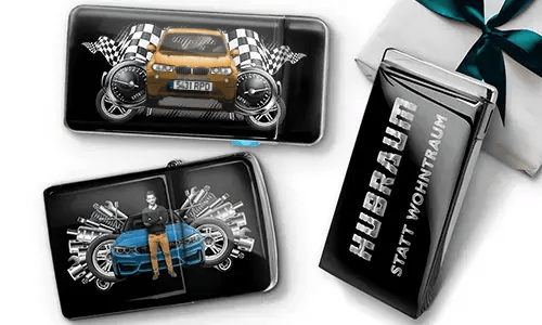 Geschenkset mit Auto-Themen-Metallbehältern, die Bilder eines grünen Sportwagens, karierten Flaggen und Motor-Motiven zeigen. Enthält ein Zigarettenetui mit der Aufschrift „Hubraum Statt Wohntraum“.