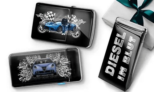 Two sleek black lighters featuring car themes, one with a blue car and checkered flags, another with a red car and gears. A third lighter reads 'DIESEL IM BLUT'. Gift-wrapped in the background.