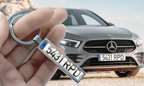 Llavero estilo placa de matrícula cómic, sostenido en la mano con la placa de coche correspondiente en el fondo