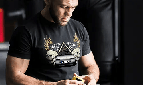 Black T-shirt with graphic of car, skulls, pistols, golden wings, and starry triangle background