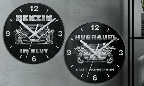 Zwei schwarze Wanduhren mit Autoillustrationen und deutschem Text: BENZIN IM BLUT und HUBRAUM STATT WOHNTRAUM
